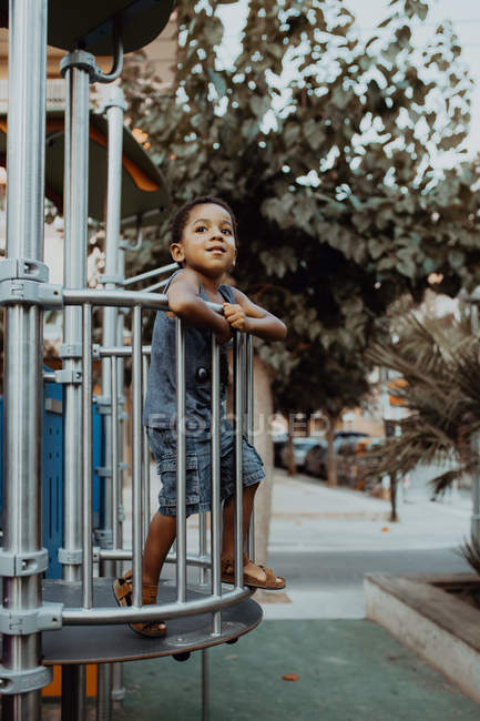 Menino afro-americano olhando para longe enquanto estava atrás da grade no playground no parque — Fotografia de Stock