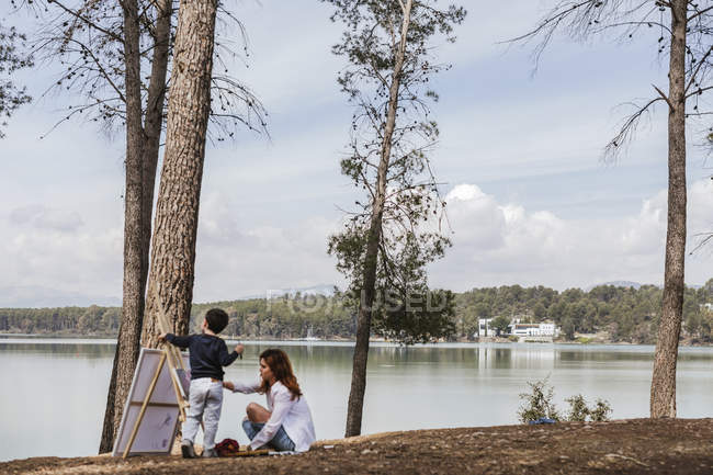 Madre y niño pintando cerca del lago - foto de stock