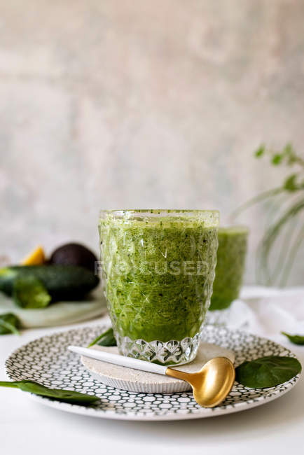 Healthy green smoothie of spinach, avocado and kiwi, apple and lemon in glass on patterned plate — Stock Photo