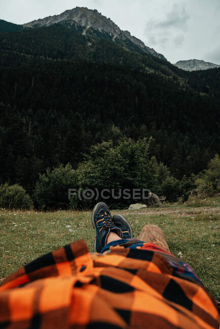Unrecognizable tourist lying on grass near majestic mountain peak in countryside — Stock Photo