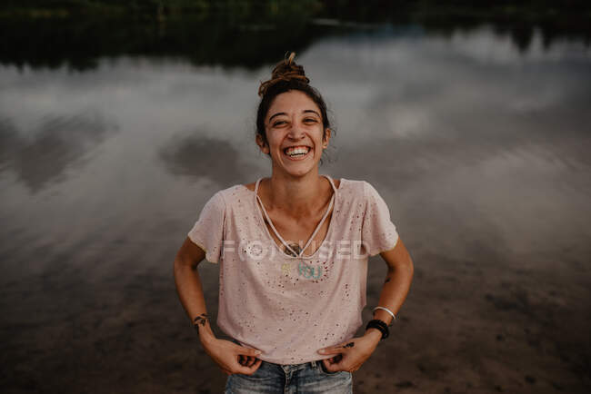 Portrait de femme souriante près d'un étang avec de l'eau calme à la campagne — Photo de stock