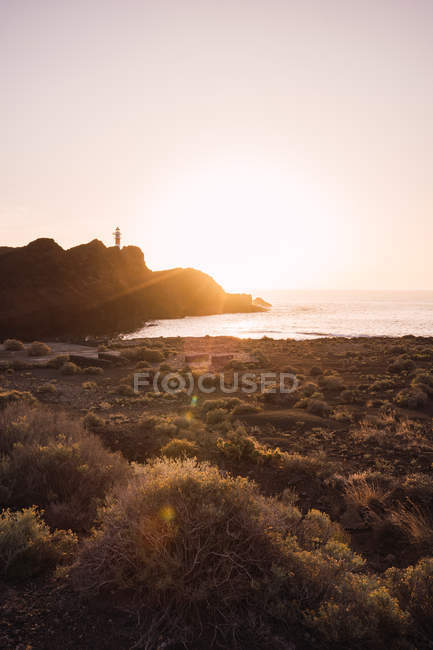 Picturesque view of stone cliff on coast in calm water with bright sunset backlit, Spain — Stock Photo