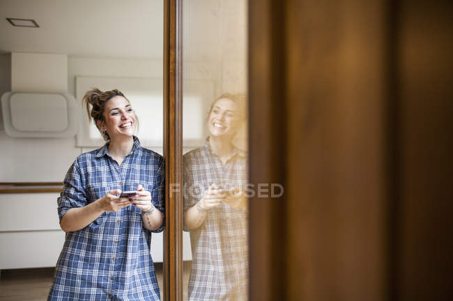 Bella e giovane donna divertendosi e chiacchierando con lo smart phone nella sua casa e sorridendo — Foto stock
