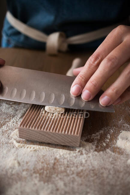 Anonymous female preparing dough for homemade gnocchetti pasta on a wooden tool in table in kitchen — Stock Photo