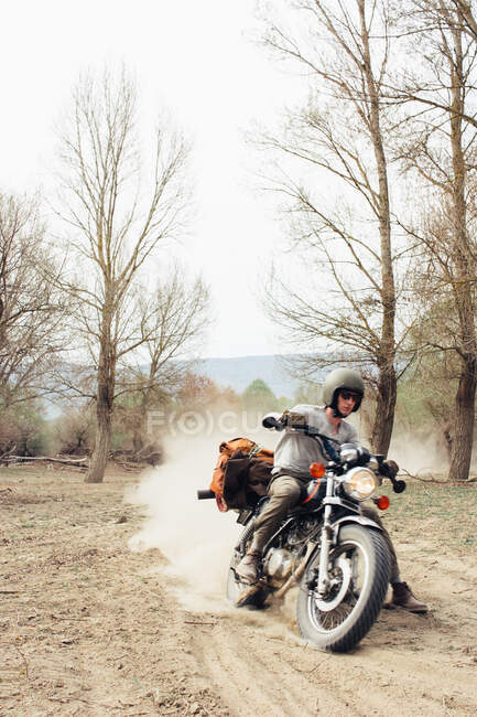 Male in helmet riding fast motorbike on dusty countryside road near leafless trees in nature — Stock Photo