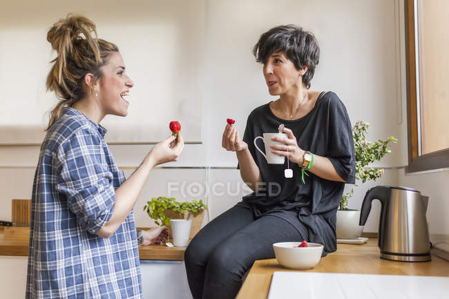 Dos mujeres hermosas y jóvenes desayunando en casa y divirtiéndose, sentadas en la cocina - foto de stock