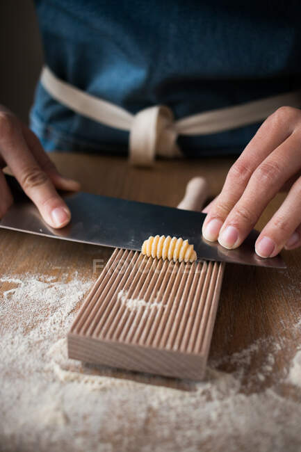 Mulher anônima preparando massa para macarrão gnocchetti caseiro em uma ferramenta de madeira na mesa na cozinha — Fotografia de Stock