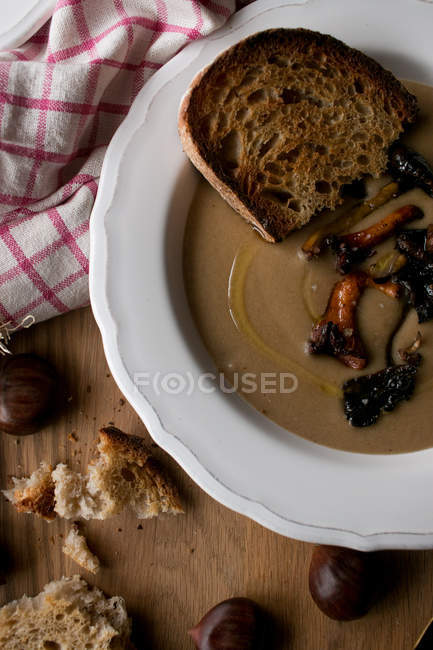 Тарелка восхитительного каштанового супа с грибами и салфеткой на деревянной столешнице . — стоковое фото