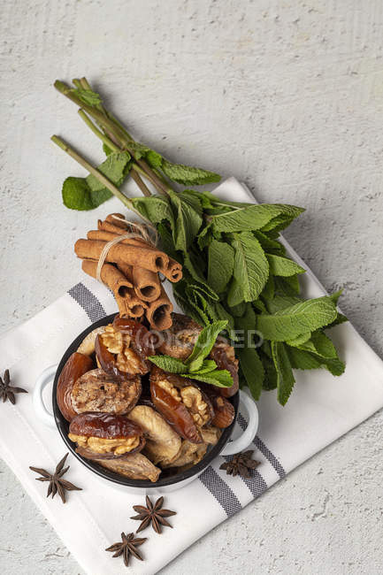 Dried dates, figs, fresh mint and cinnamon for halal snack for Ramadan in pot on kitchen towel — Stock Photo