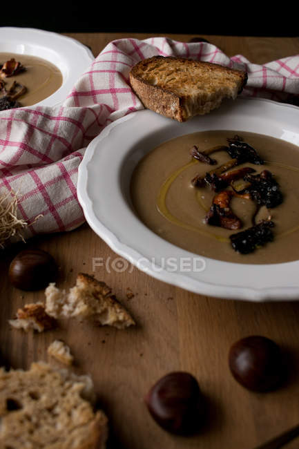 Platos de deliciosa sopa de castañas con champiñones y servilleta sobre mesa de madera . - foto de stock