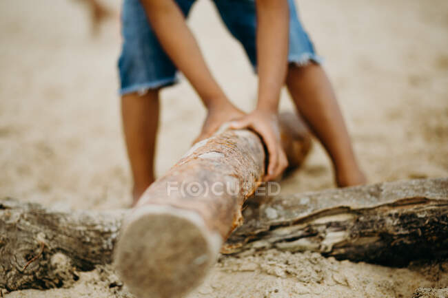 Crop African American boy with stick playing on sandy shore near sea — Stock Photo