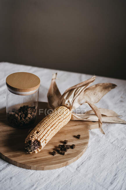 Сушена кукурудза на коб поміщається на дерев'яну дошку біля банки з коричневою спецією на кухонному столі — стокове фото