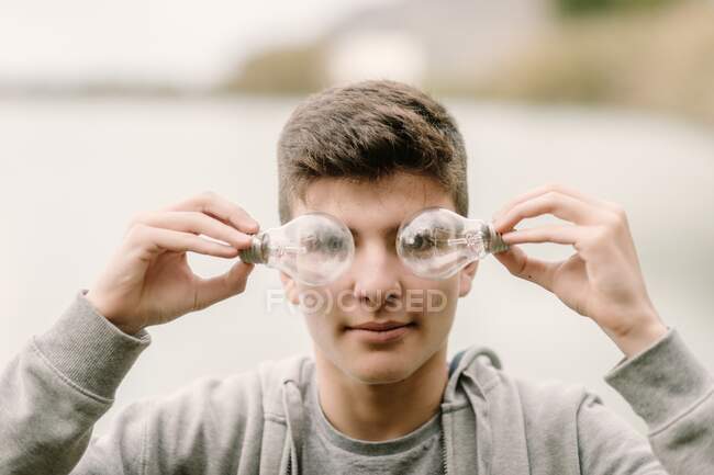 Young teenager boy with a couple of light bulbs in front of his eyes innovation and imagination concept — Stock Photo
