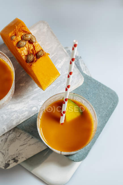 Mango and pumpkin smoothie in glass on stacked boards on white background — Stock Photo