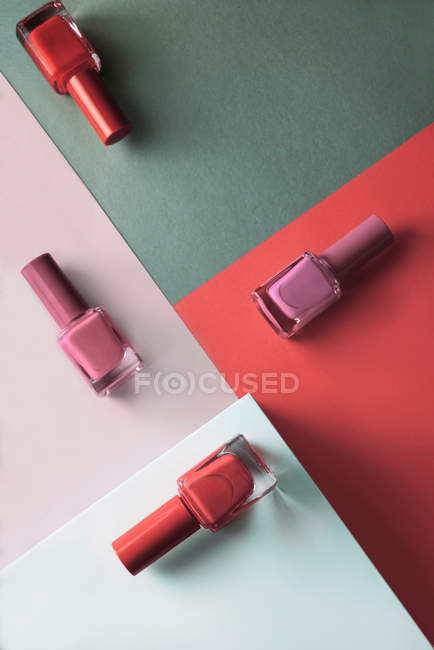 Esmaltes de uñas multicolores sobre fondo de patrón geométrico de colores - foto de stock