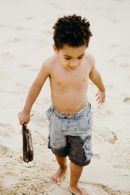 Lustiger afroamerikanischer Junge mit Stock spielt am Sandstrand in der Nähe des Meeres — Stockfoto