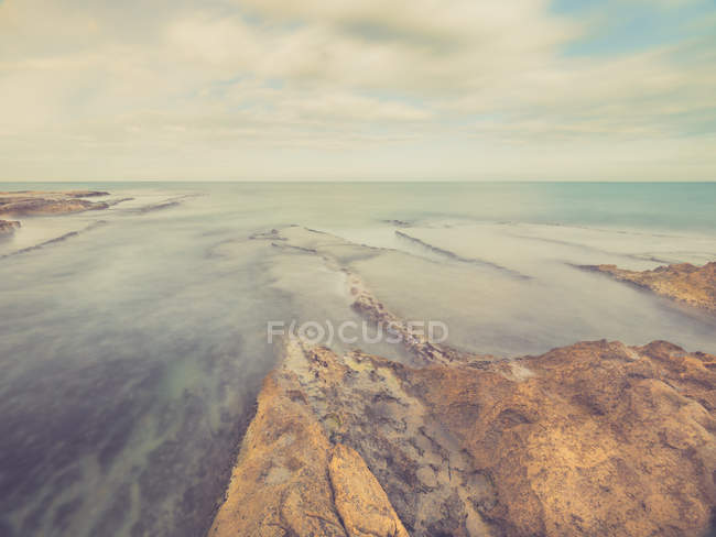 Costa rocosa y mar azul espumoso en el fondo del cielo con nubes - foto de stock