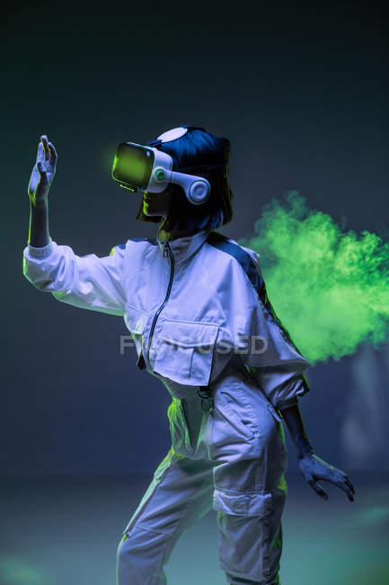 Jovem excitada tocando o ar enquanto tem experiência de realidade virtual em luz de néon — Fotografia de Stock