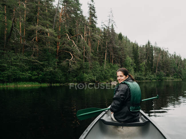 Jovem mulher sorridente olhando para trás enquanto passeia de barco no rio da floresta na Finlândia — Fotografia de Stock