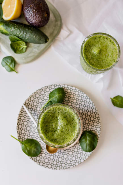 Batido verde saludable de espinacas, aguacate y kiwi, manzana y limón en vasos sobre mesa blanca con ingredientes - foto de stock