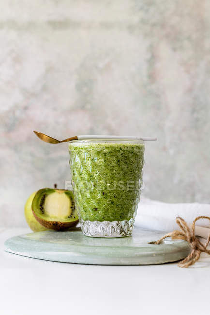 Healthy green smoothie of spinach, avocado and kiwi, apple and lemon in glass on wooden board — Stock Photo