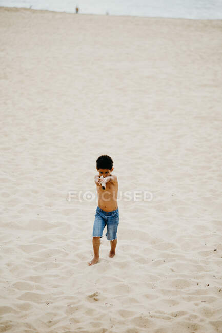 Drôle afro-américain garçon avec bâton jouer sur le rivage sablonneux près de la mer — Photo de stock
