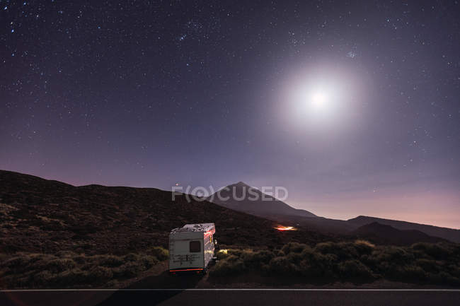 Camper trailer parked on roadside of remote desert under stunning glowing moon and starry sky — Stock Photo