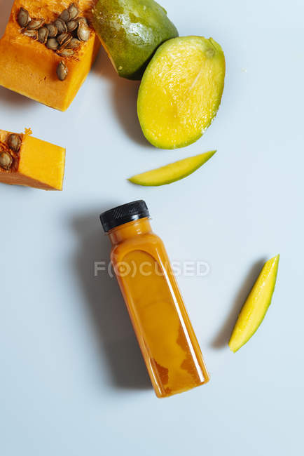 Smoothie végétalien à la mangue et à la citrouille en bouteille sur fond blanc avec ingrédients — Photo de stock