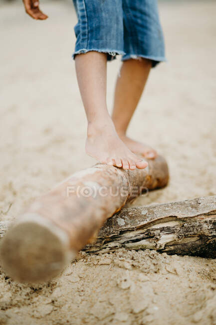 Грязные ноги неузнаваемого черного ребенка, идущего по бревно по песчаному пляжу — стоковое фото