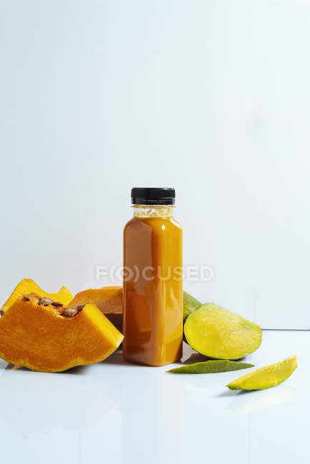 Batido vegano de mango y calabaza en botella sobre fondo blanco con ingredientes - foto de stock