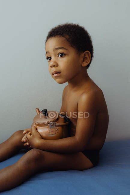 Kind sitzt in gemütlichem Bett im Zimmer mit Teekanne — Stockfoto