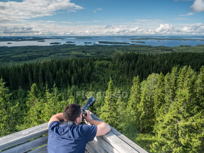 Back view of young man taking photos of beautiful landscape on digital camera in Finland — Stock Photo