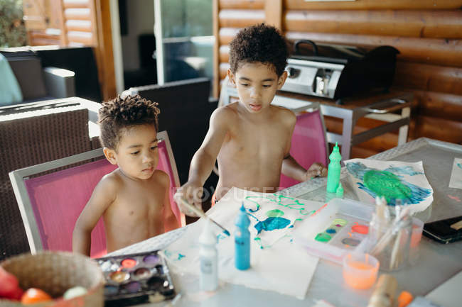 Zwei hemdlose afrikanisch-amerikanische Jungen mit heller Farbe abstrakte Bilder auf dem Tisch zu Hause zu machen — Stockfoto