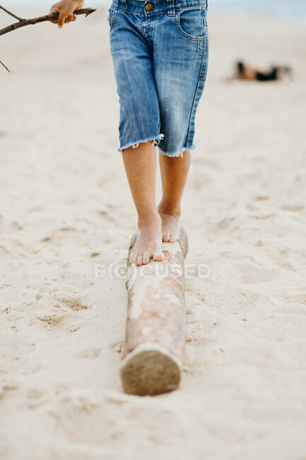Schmutzige Beine eines bis zur Unkenntlichkeit schwarzen Kindes, das auf Baumstämmen am Sandstrand spaziert — Stockfoto