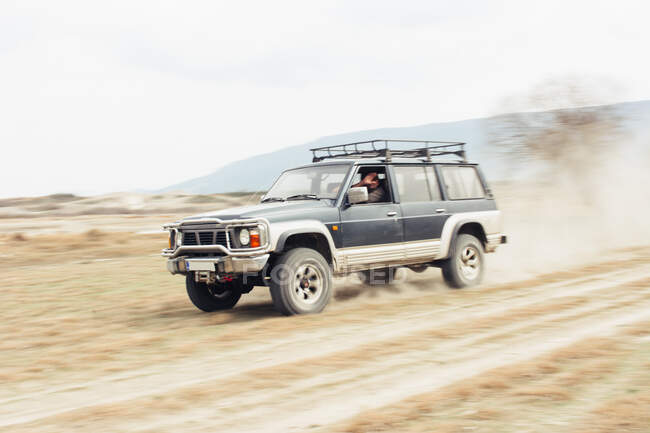 Off road car riding on dusty road near leafless trees during trip through countryside — Stock Photo