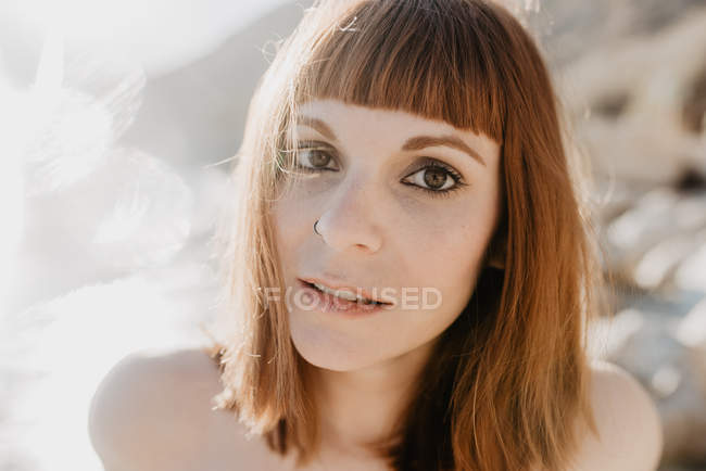 Macchie di luce solare brillante di fronte alla donna nuda che guarda la fotocamera contro il cielo senza nuvole in natura — Foto stock