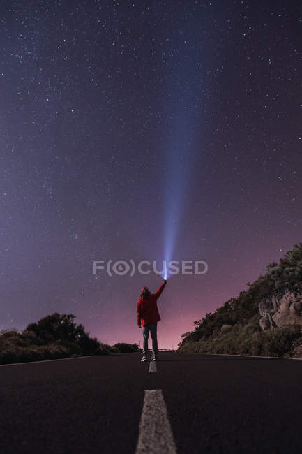 Viaggiatore in giacca rossa con cappuccio in piedi con torcia nella notte stellata — Foto stock