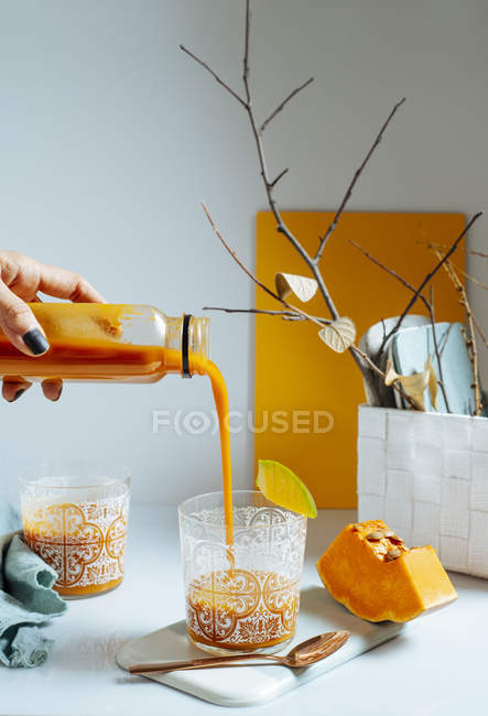 Female hand serving fresh mango smoothie into glasses on white table — Stock Photo