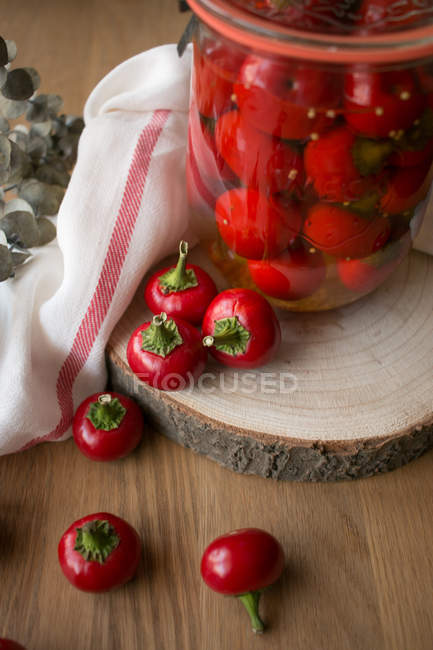 Натюрморт с банкой вкусного маринованного перца pimientos помещен на кусок дерева рядом с салфеткой и веточкой растения . — стоковое фото