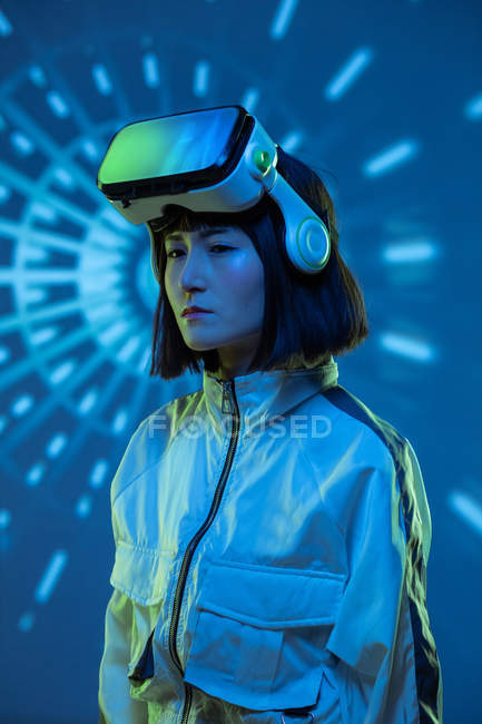 Giovane donna con occhiali di realtà virtuale guardando lontano in luce al neon — Foto stock