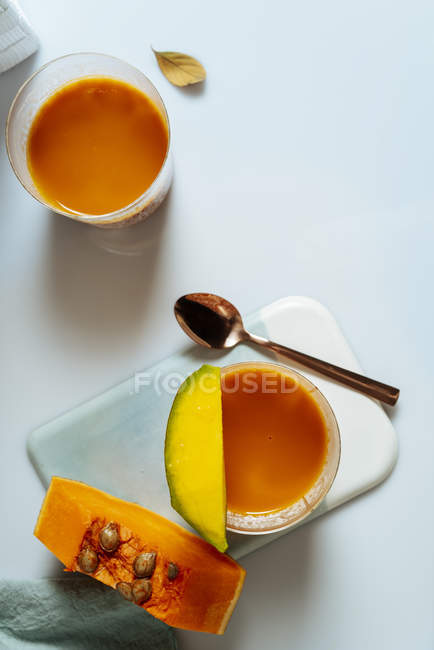 Batido de mango y calabaza en vidrio sobre fondo blanco con ingredientes - foto de stock