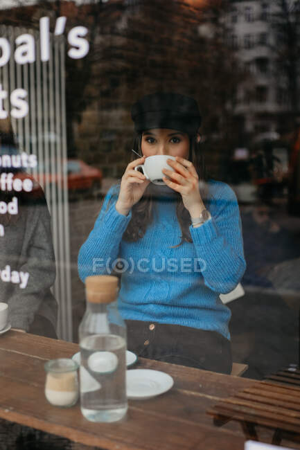 Зовні фото стильної жінки, яка п'є каву в кав'ярню, дивлячись далеко — стокове фото