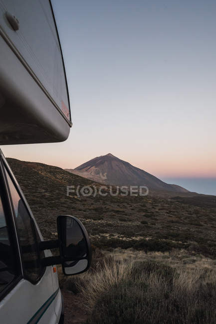 Кемпер припаркований в дикій місцевості на тлі гірського піку і світанкового неба вранці — стокове фото