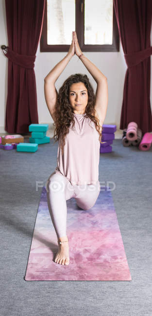 Flexible sportliche Brünette macht Yoga-Pose mit den Händen über dem Kopf und blickt in die Kamera — Stockfoto