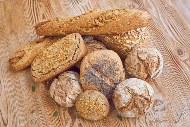 Сверху композиция свежего горячего вкусного хлеба хлебов, булочек и багетов на деревянном столе в пекарне — стоковое фото