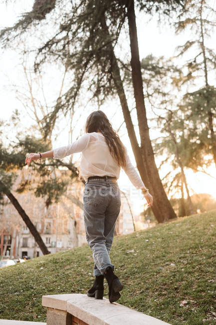 Young female in casual outfit stretching out arms balancing on fence on sunny day in park — Stock Photo