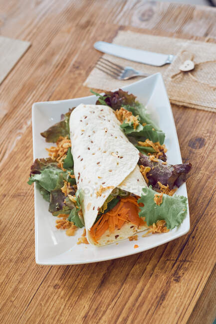 Rolo vegetariano cozido apetitoso com cenoura fresca saudável e salada na placa branca na mesa de madeira no café — Fotografia de Stock