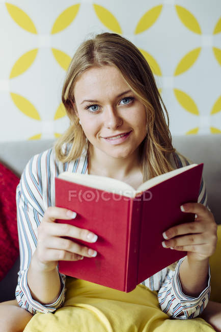 Jeune femme heureuse livre de lecture sur canapé — Photo de stock