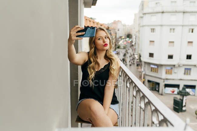 Молода усміхнена жінка бере селфі на терасі — стокове фото