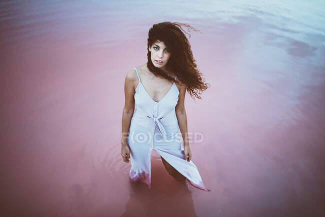 Jovem mulher bonita com cabelos longos encaracolados usando vestido de verão apreciando brisa do mar — Fotografia de Stock